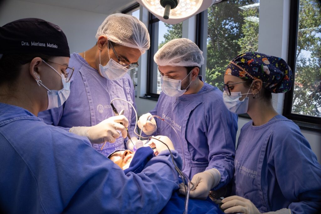 Equipe médica cirúrgica devidamente paramentada realizando um procedimento reconstrutivo de alta complexidade dentro do centro cirúrgico do Hospital SOBRAPAR.
